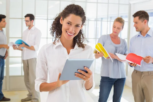 Mulher de negócios casual usando tablet com equipe atrás dela — Fotografia de Stock