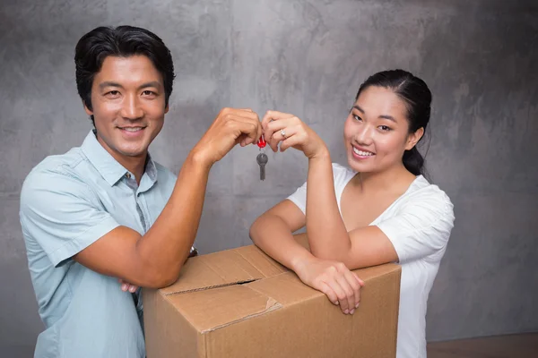 Happy couple holding house key and leaning on moving box — Stock Photo, Image