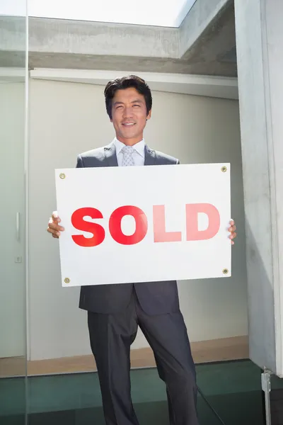 Säker fastighetsmäklare står vid ytterdörren som visar säljs tecken — Stockfoto