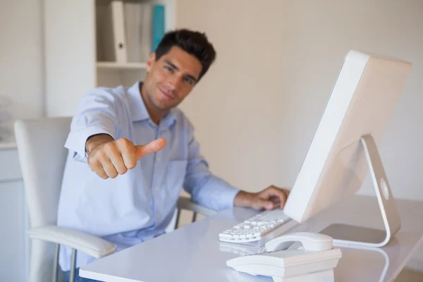 Casual businessman giving thumbs up to camera at his desk — Stock Photo, Image