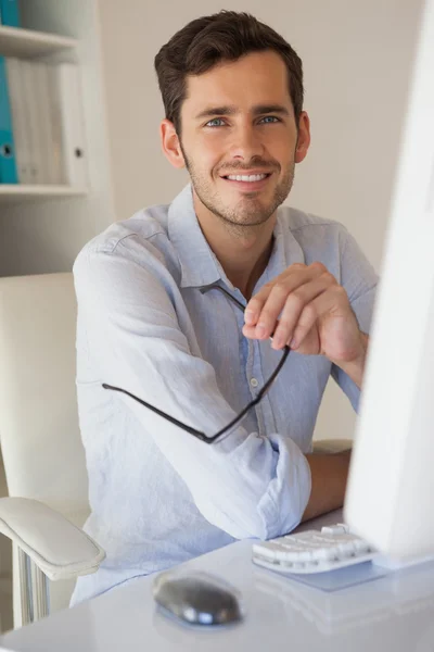 Casual businessman smiling at camera at his desk — Stock Photo, Image