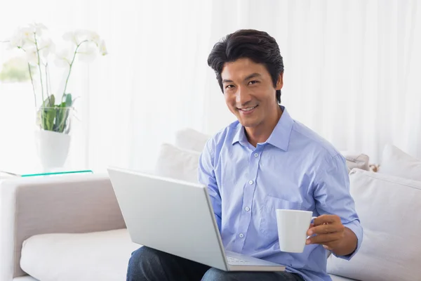 Glücklicher Mann sitzt mit Laptop auf Couch und trinkt Kaffee — Stockfoto