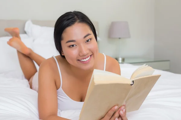 Donna sorridente sdraiata sul letto a leggere — Foto Stock