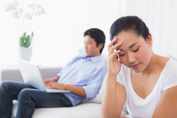 Upset woman sitting on couch while boyfriend uses laptop — Stock Photo, Image