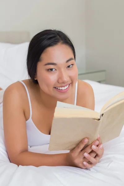 Улыбающаяся женщина лежит на кровати и читает — стоковое фото