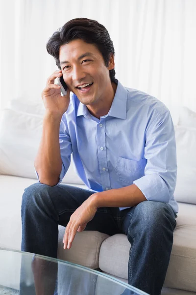 Homem feliz sentado no sofá falando ao telefone — Fotografia de Stock
