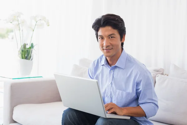 Lycklig man sitter på soffan med laptop — Stockfoto