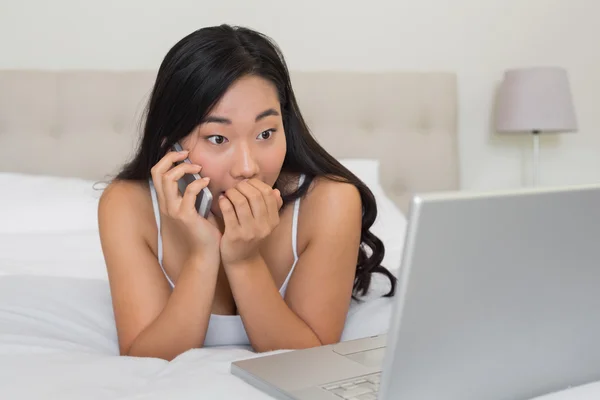 Chockad kvinna som tittar på laptop på telefonen — Stockfoto