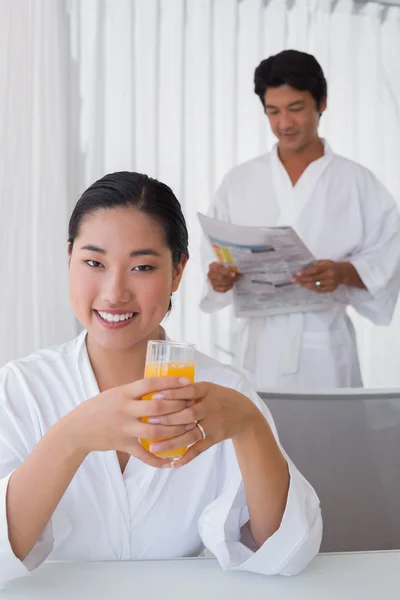 Woman in bathrobe having orange juice with boyfriend in background — Stock Photo, Image