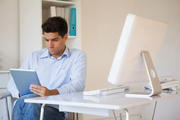 Casual affärsman med sin tablett vid sitt skrivbord — Stockfoto