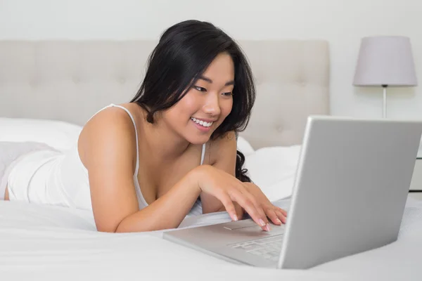 Mujer feliz acostada en la cama usando portátil —  Fotos de Stock