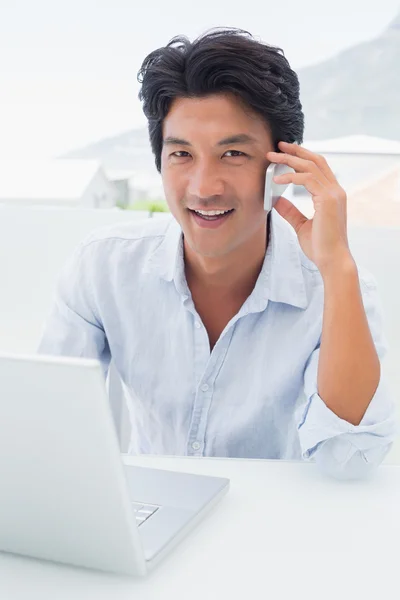 Lächelnder Mann, der seinen Laptop benutzt und telefoniert — Stockfoto