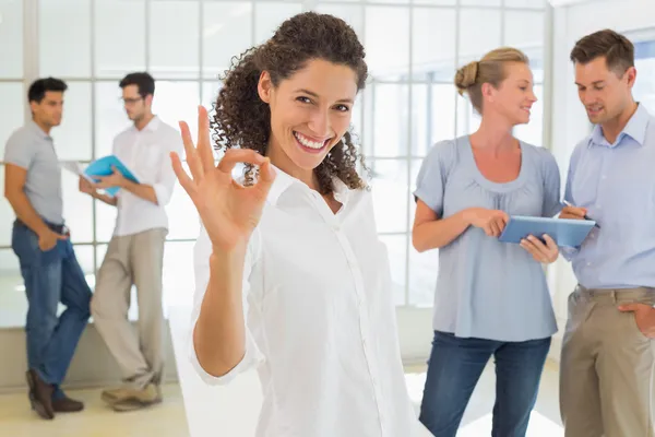 Casual businesswoman giving ok sign to camera — Stock Photo, Image