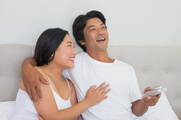 Sorrindo asiático casal deitado na cama assistindo tv — Fotografia de Stock