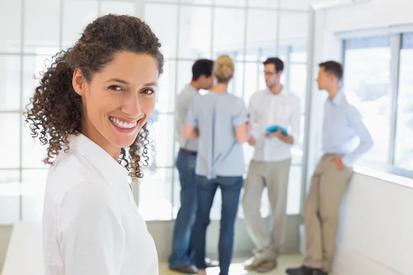 Gelegenheitsunternehmerin lächelt mit Team im Rücken in die Kamera — Stockfoto