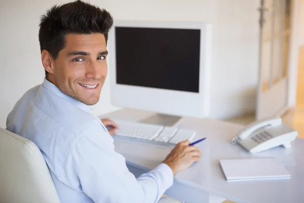 Lässiger Geschäftsmann am Schreibtisch lächelt in die Kamera — Stockfoto