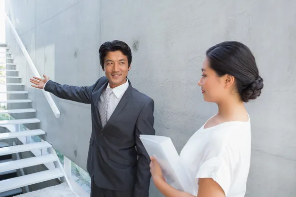 Estate agent showing stairs to customer and smiling — Stock Photo, Image