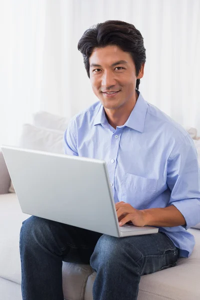 Lycklig man sitter på soffan med laptop — Stockfoto