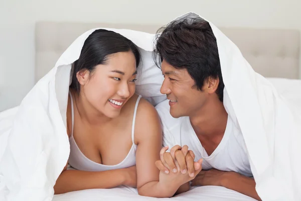 Happy couple lying on bed together under the duvet — Stock Photo, Image