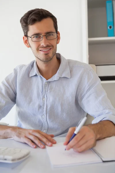 Casual smiling businessman taking notes at his desk — Stock Photo, Image