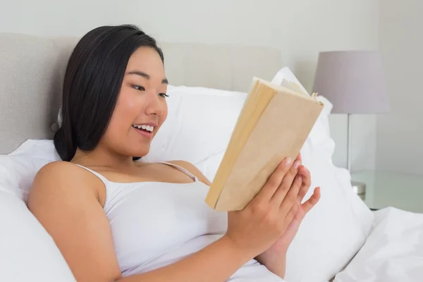Χαμογελώντας γυναίκα ξαπλωμένη στο κρεβάτι ανάγνωση — Φωτογραφία Αρχείου