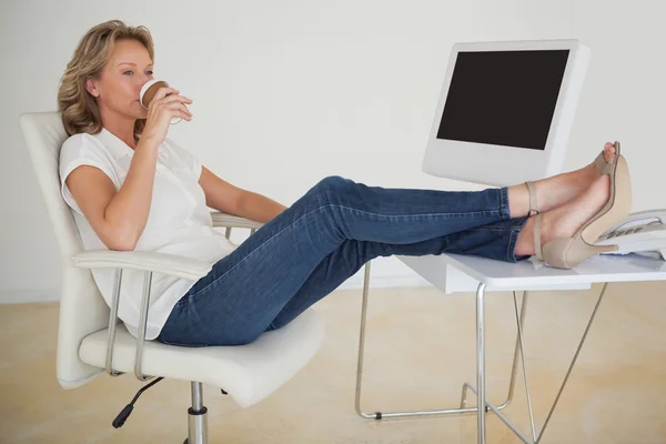 Mujer de negocios casual tomando un café con los pies en el escritorio — Foto de Stock