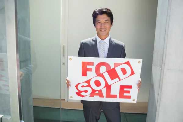 Agent immobilier confiant debout à la porte d'entrée montrant panneau vendu — Photo