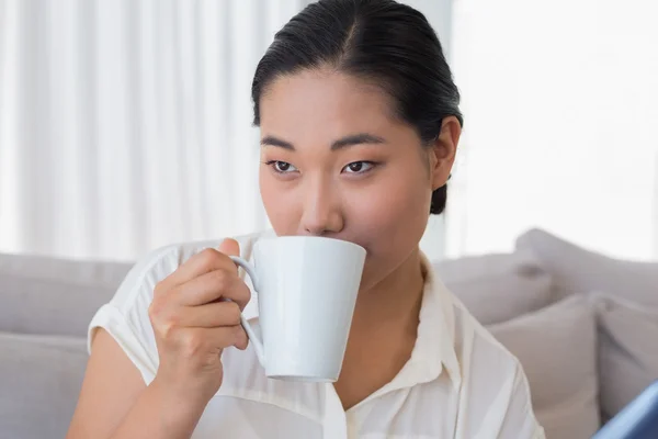 コーヒーを飲んでいるソファに座っている女性の笑みを浮かべてください。 — ストック写真