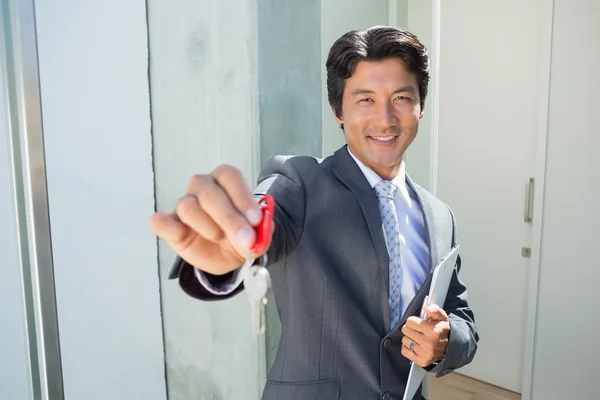 Confident estate agent standing at front door showing key — Stock Photo, Image