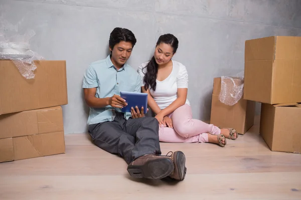 Pareja feliz sentada en el suelo usando una tableta rodeada de cajas — Foto de Stock