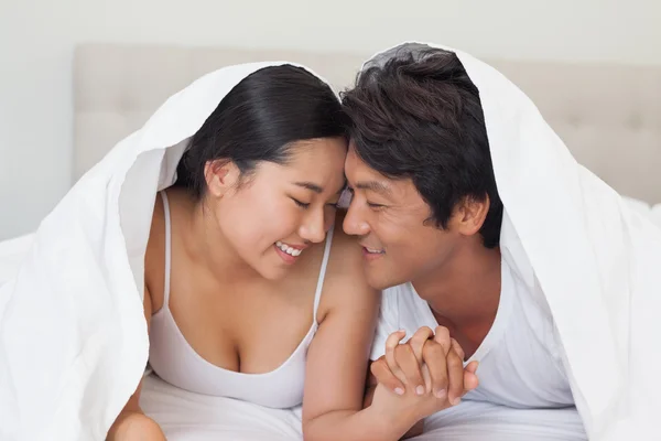 Happy couple lying on bed together under the duvet — Stock Photo, Image