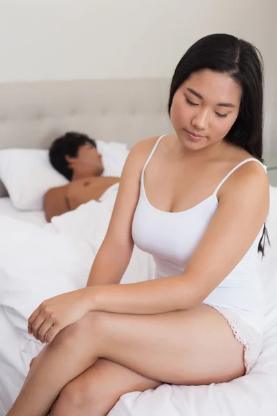Woman sitting on end of bed as boyfriend sleeps — Stock Photo, Image