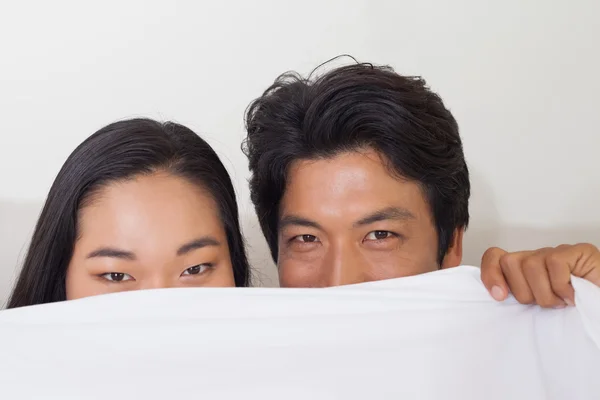 Happy couple holding duvet over face — Stock Photo, Image
