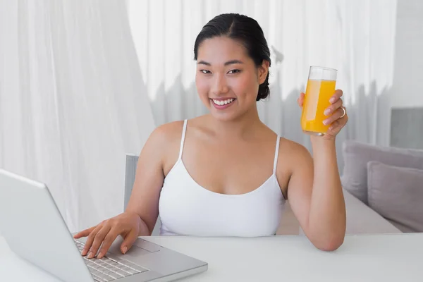 Mujer feliz usando el ordenador portátil y tener jugo de naranja —  Fotos de Stock