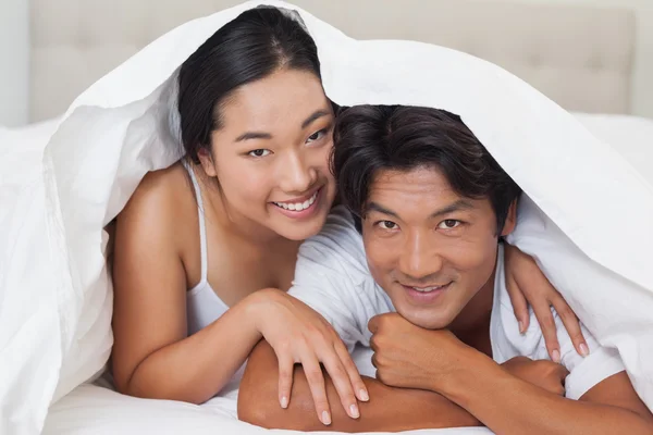 Happy couple lying on bed together under the duvet — Stock Photo, Image