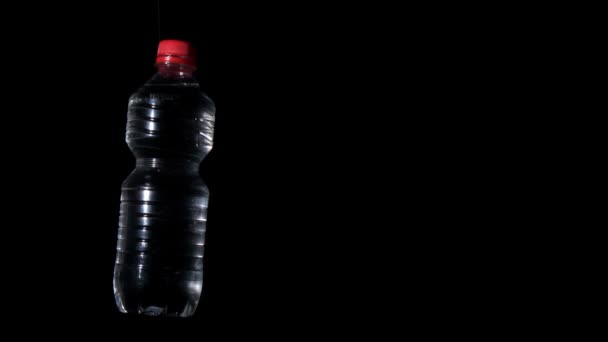 Пластиковая бутылка вращается на черной поверхности — стоковое видео
