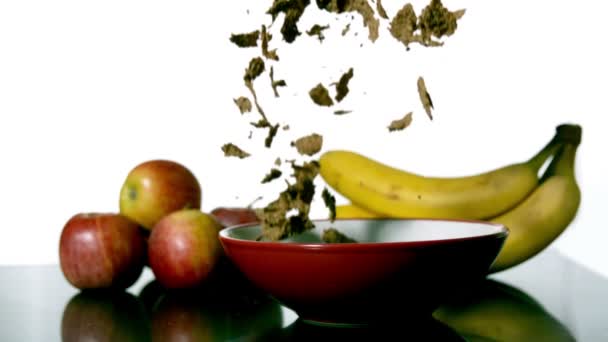 Cereais caindo em uma tigela ao lado de frutas — Vídeo de Stock