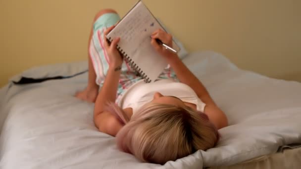 Blondynka pisania w notatniku na jej łóżko — Wideo stockowe