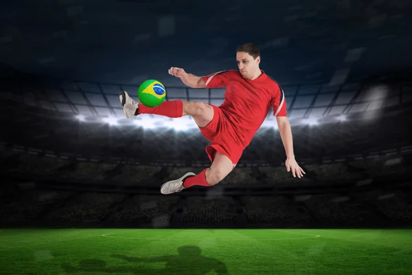 Composite image of fit football player jumping and kicking — Stock Photo, Image