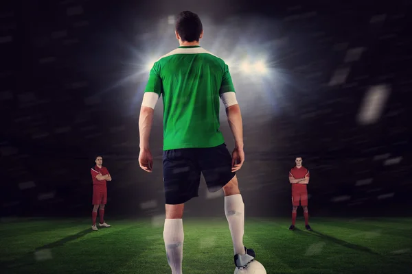 Футболист в зеленом с мячом лицом к оппозиции — стоковое фото