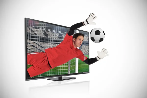 Composite image of fit goal keeper saving goal through tv — Stock Photo, Image