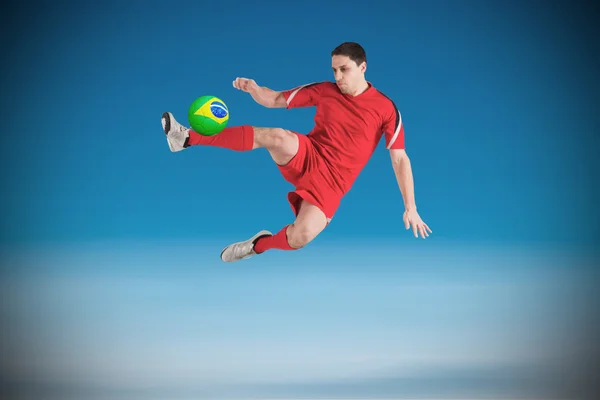 Composite image of fit football player jumping and kicking — Stock Photo, Image