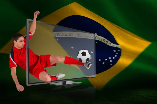 Imagem composta do jogador de futebol apto chutando bola através da tv — Fotografia de Stock