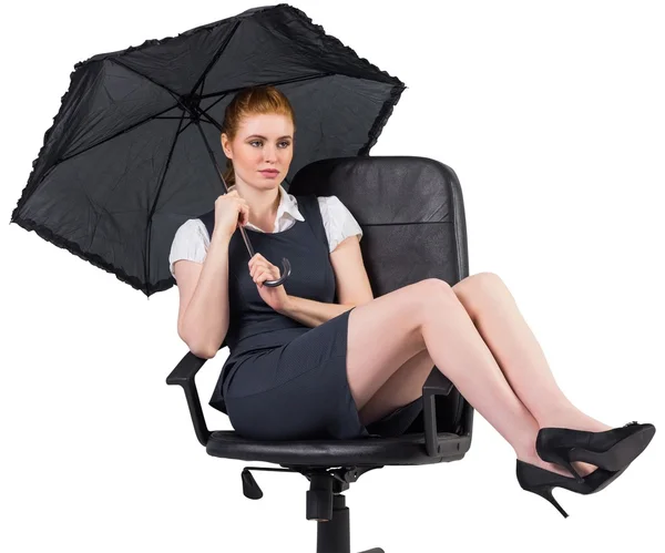 Businesswoman holding umbrella sitting on chair — Stock Photo, Image