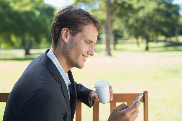 Podnikatel SMS na telefonu na lavičce v parku — Stock fotografie