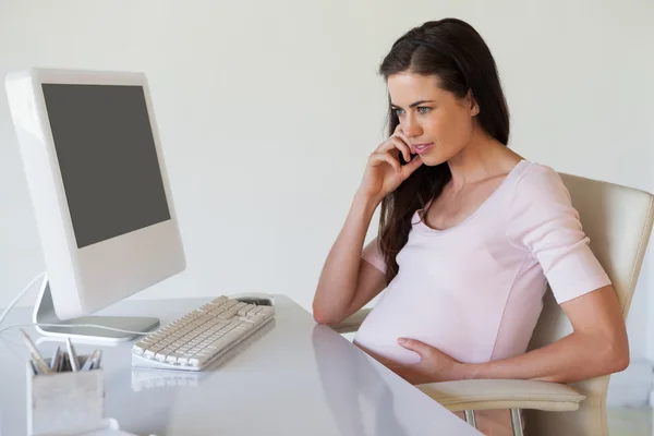 Embarazada mujer de negocios pensando en su escritorio — Foto de Stock