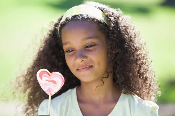 Chica sosteniendo una piruleta corazón en el parque —  Fotos de Stock