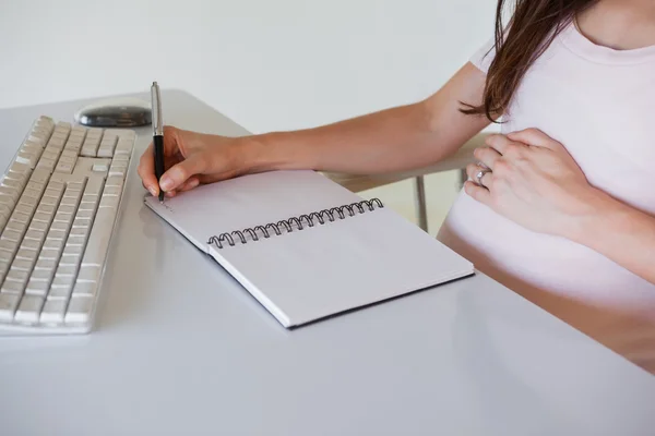 Беременная деловая женщина пишет за своим столом — стоковое фото