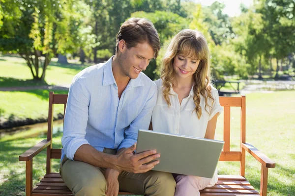 Casal no banco do parque olhando para laptop — Fotografia de Stock