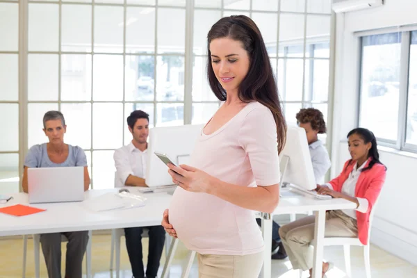 Pregnant office worker texts on phone — Stock Photo, Image